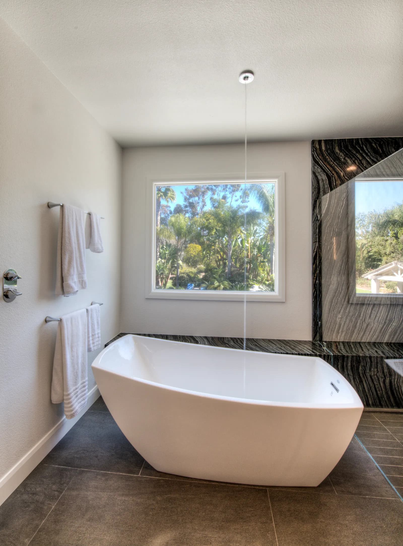 Freestanding white tub with ceiling-mounted filler, garden window and dark marble shower surround.