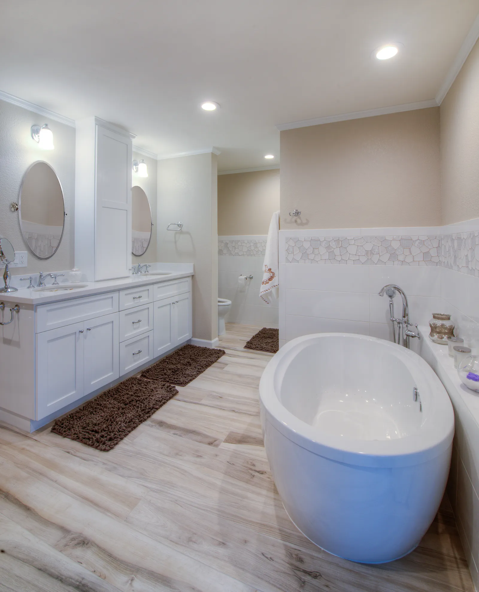 Master bathroom with a freestanding oval tub, floor-mounted filler, white double vanity, and wood-look tile floor.