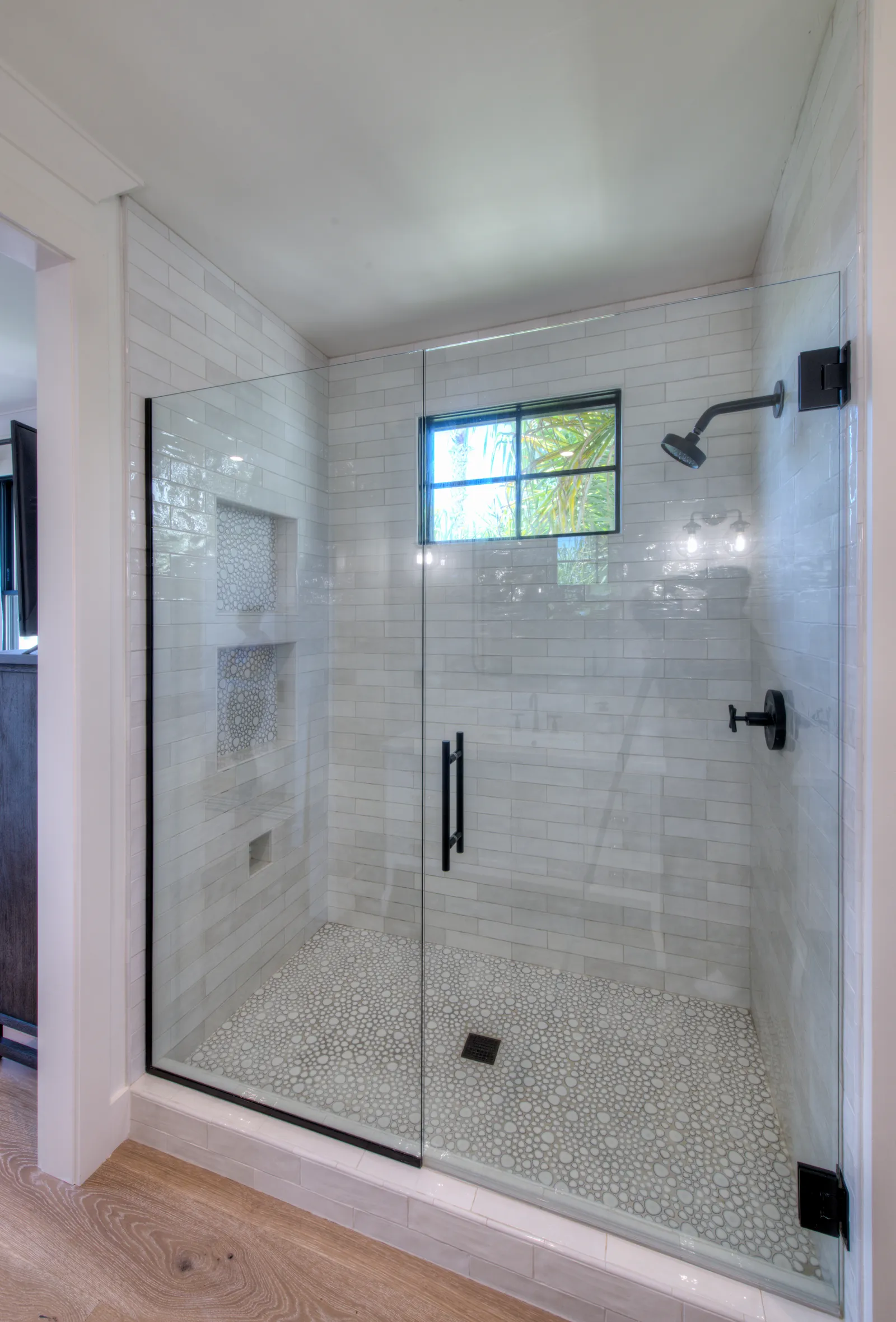 Walk-in shower with white subway tile, pebble mosaic floor, matte black fixtures, and a frameless glass door.