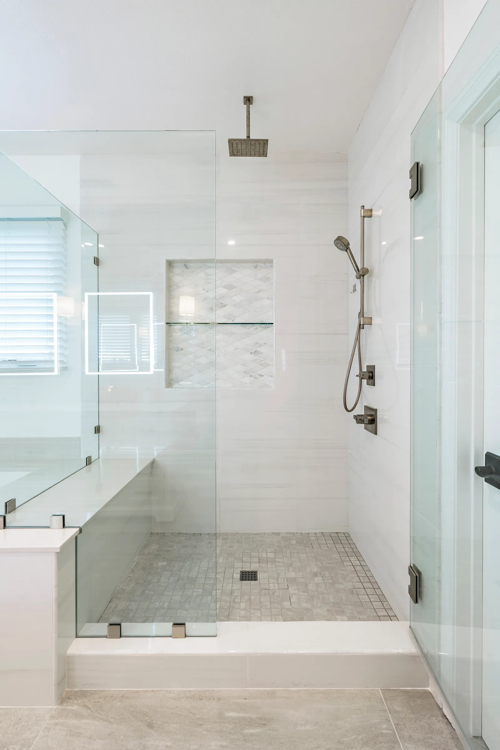 Walk-in shower with frameless glass, rain head, mosaic niche and marble-look wall tile.