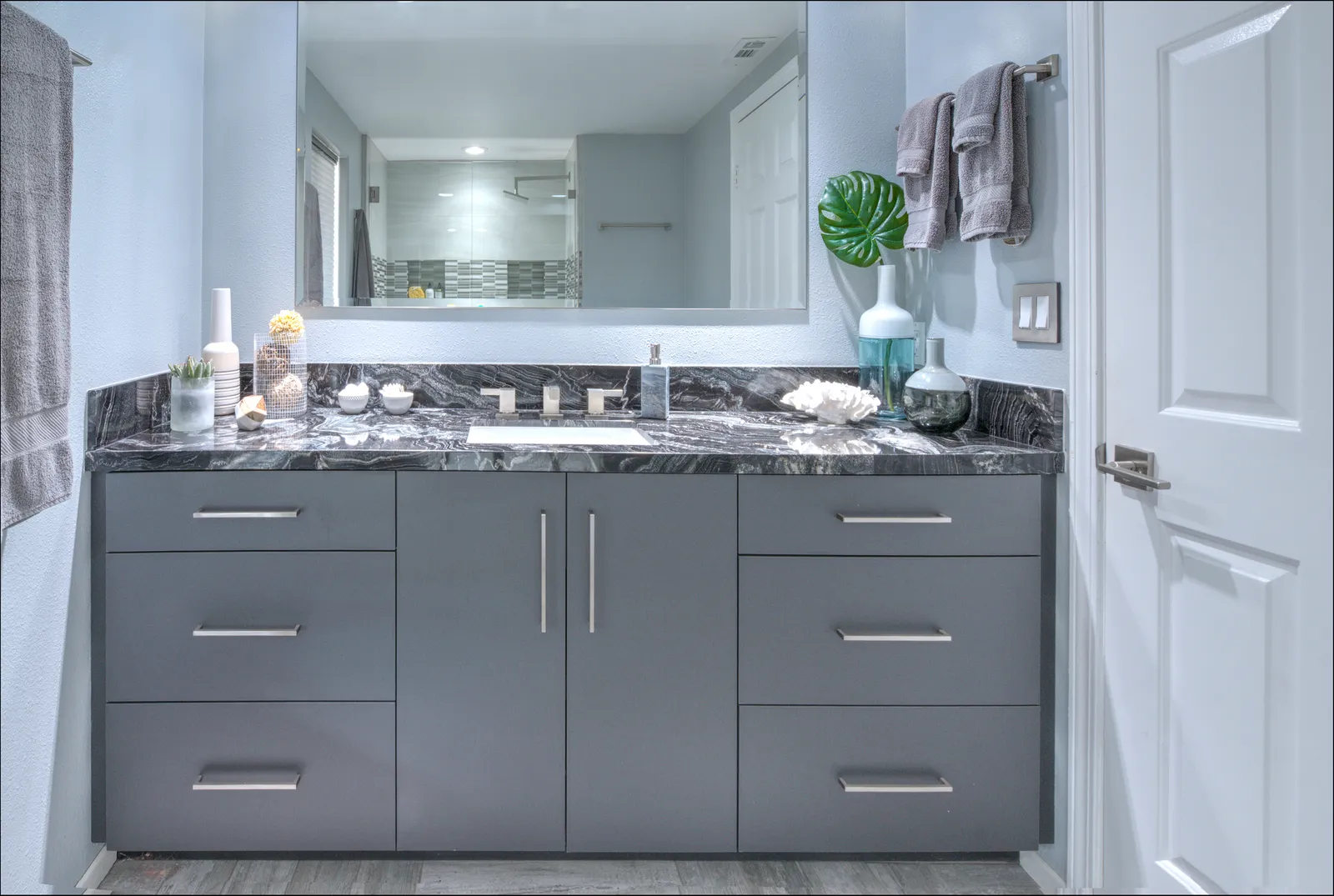 A modern bathroom vanity with flat-panel gray cabinets, a dramatic black-and-white marble countertop, and a large framed mirror.