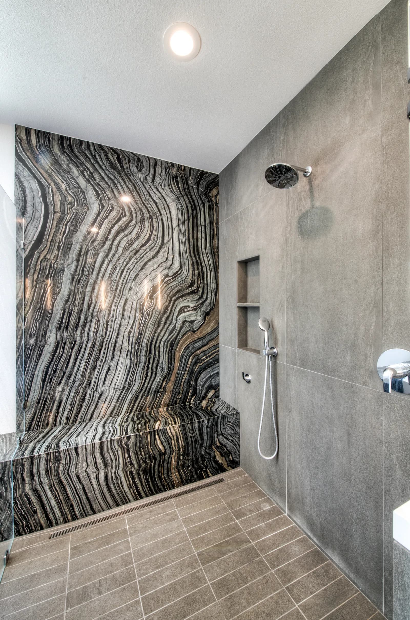 Walk-in shower with a dramatic book-matched marble feature wall, gray tile, rain head, and built-in niche.