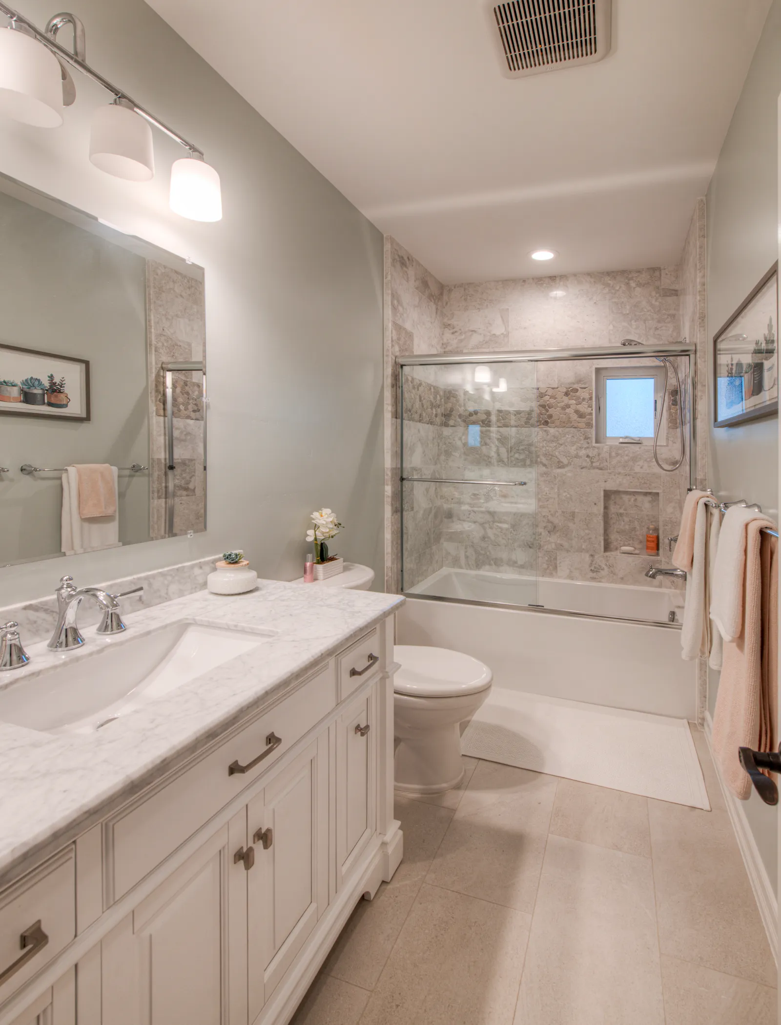 Bathroom with a white furniture-style vanity, Carrara marble top, and a tub-shower combo with stone tile surround and sliding glass doors.