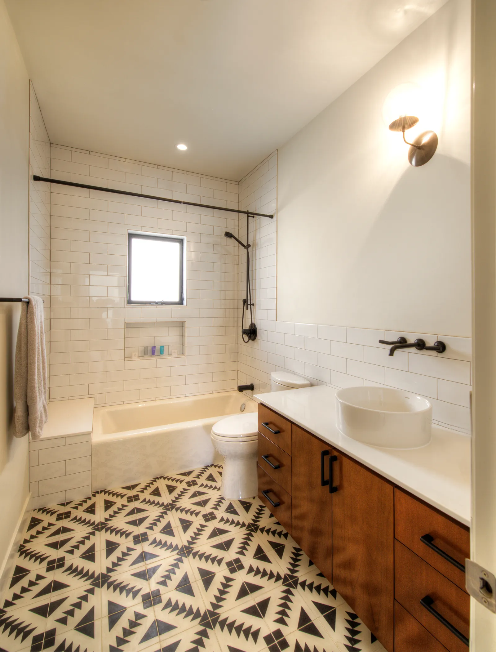 Bathroom with bold black-and-white patterned floor tile, a wood vanity with vessel sink, and a subway-tiled tub with black fixtures.