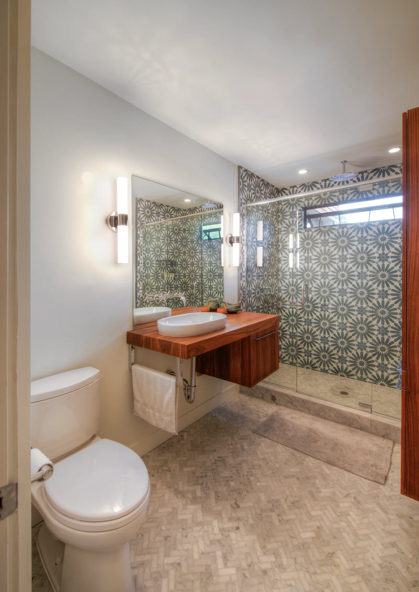 Bathroom with a glass-enclosed shower wrapped in blue floral patterned tile and a floating walnut vanity with a vessel sink.
