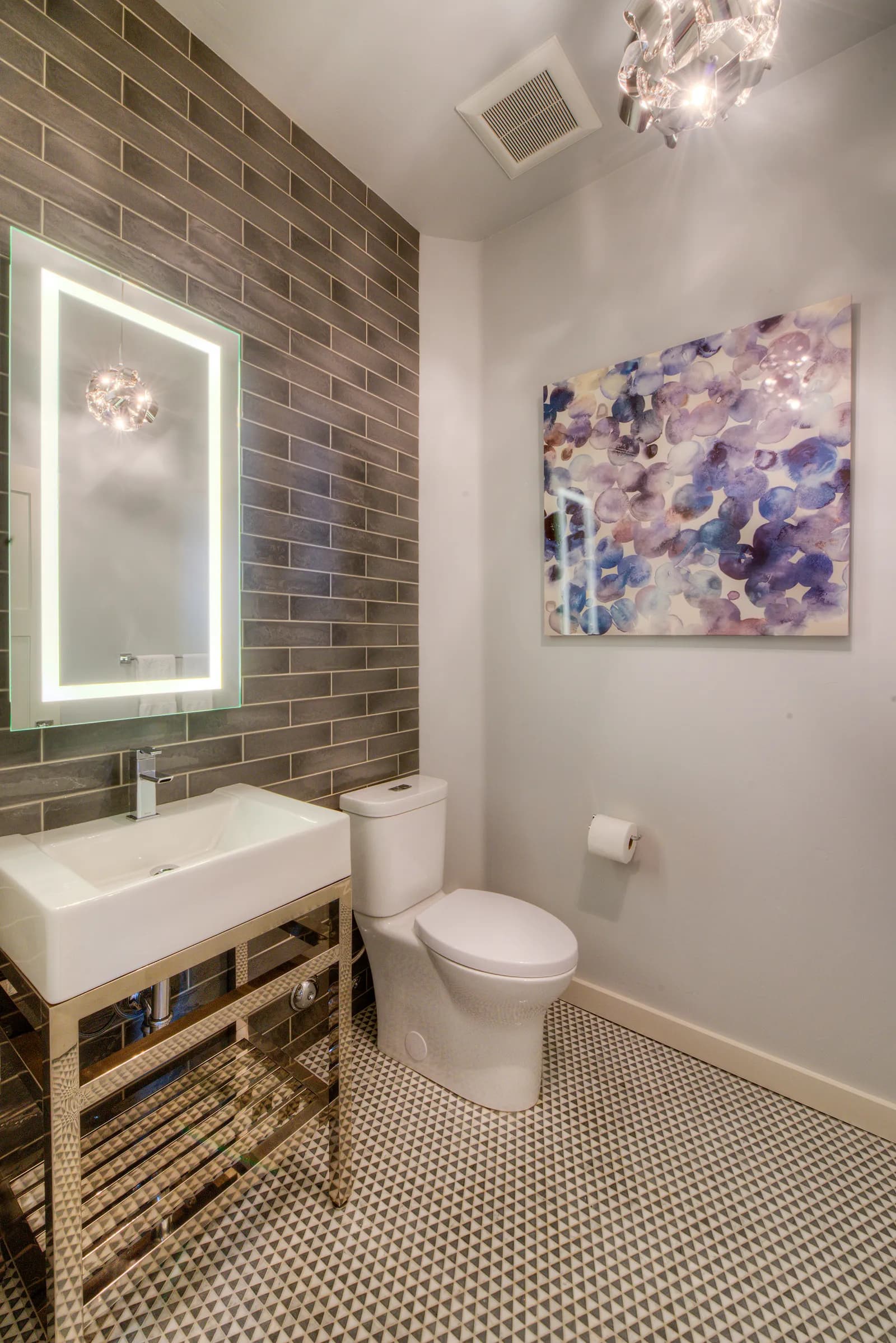 A powder room with a gray subway tile accent wall, lighted mirror, and metal console sink.