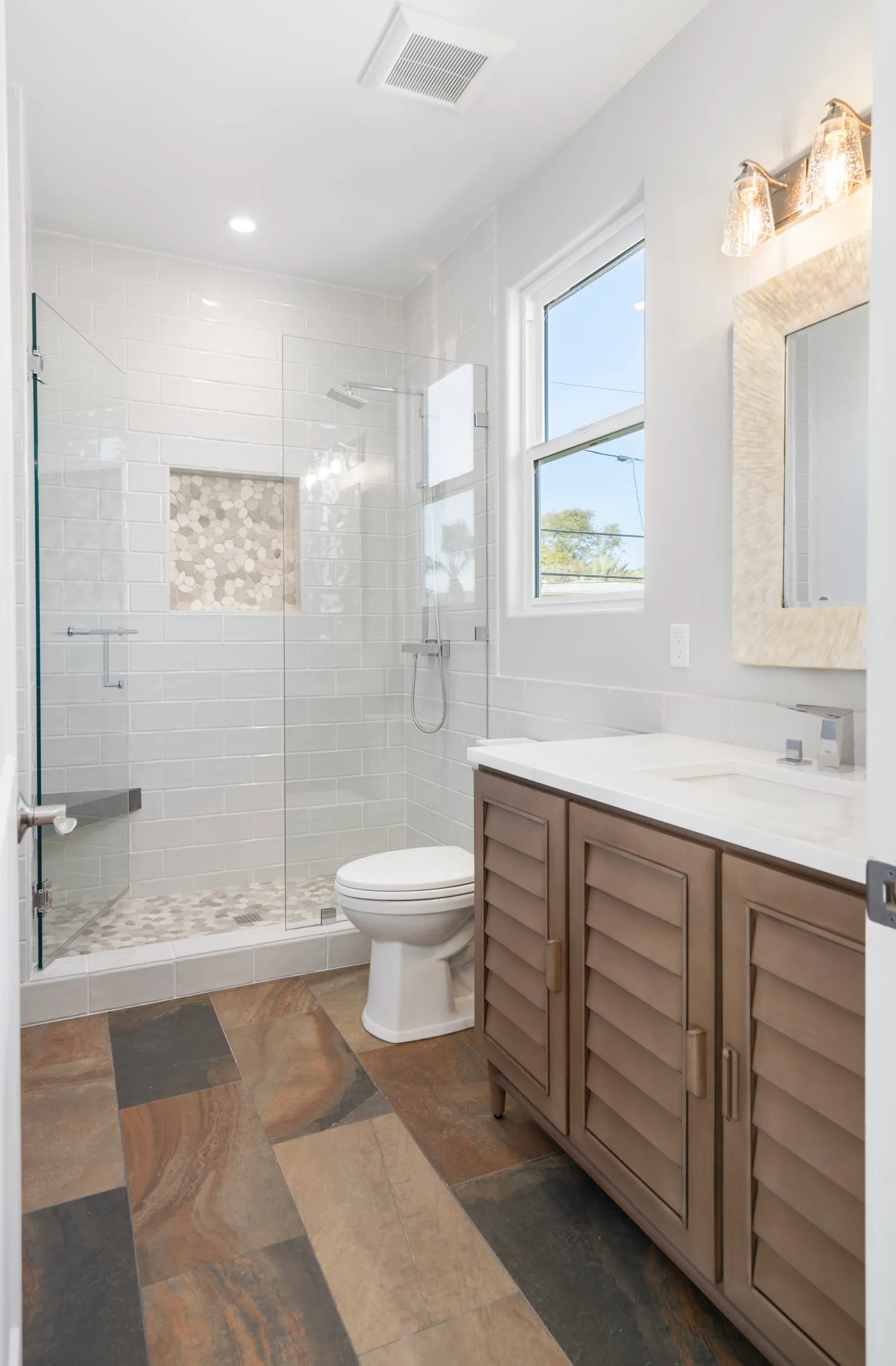 Bathroom with a glass walk-in shower in white subway tile, pebble accents, and a wood-look tile floor.