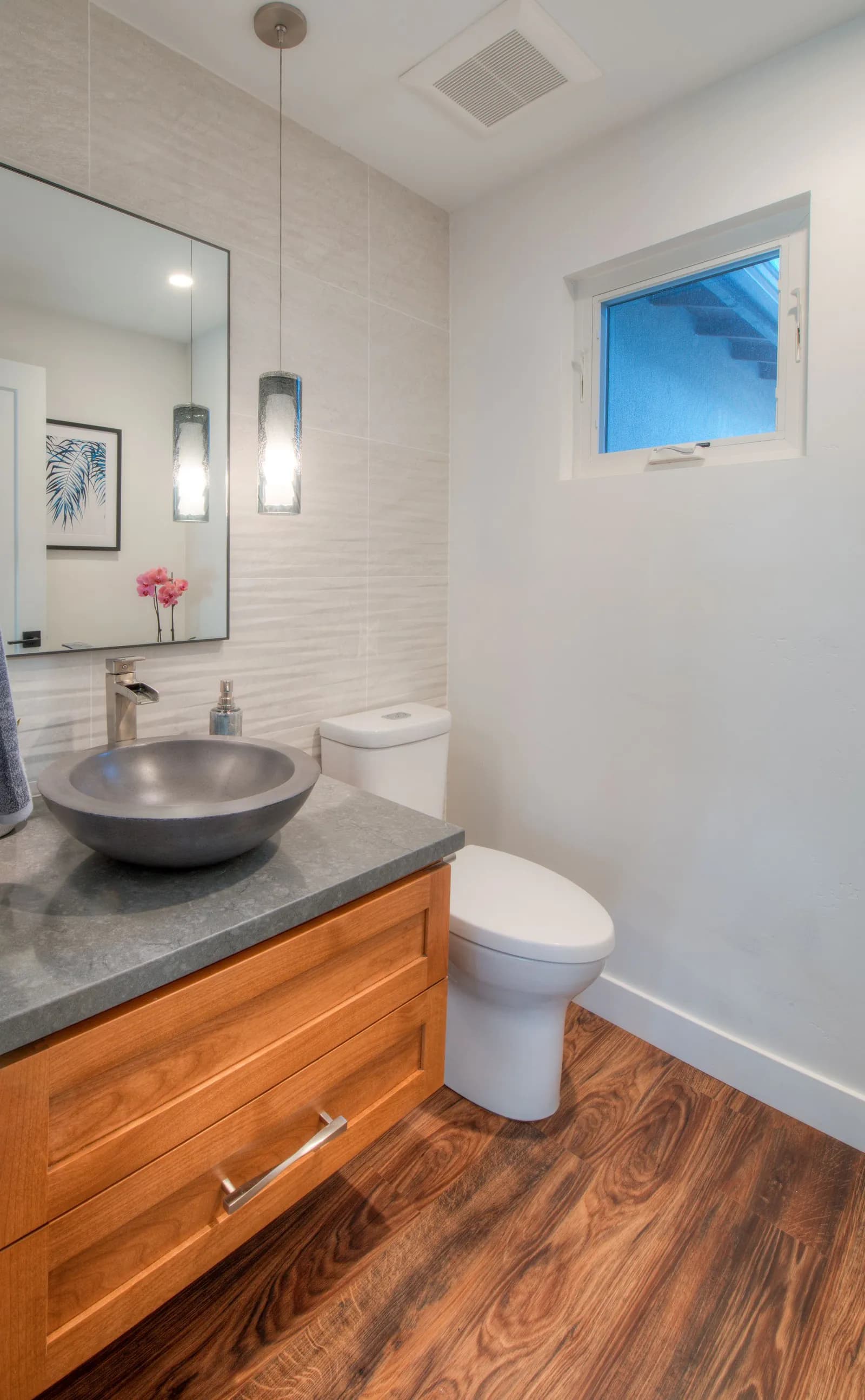 Powder room with a gray stone vessel sink, waterfall faucet, wood vanity, and a glass pendant light.