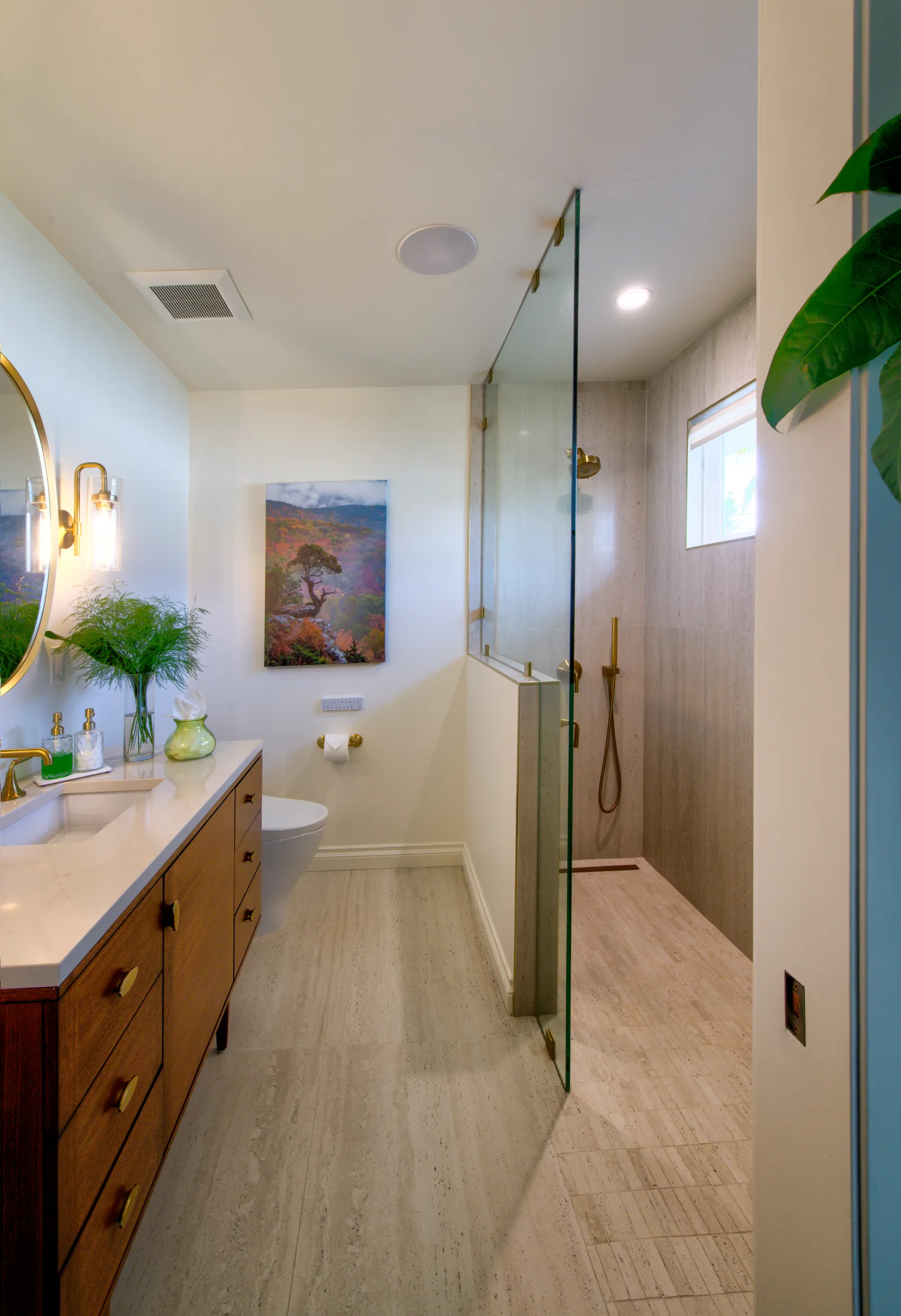 Bathroom with a glass-partitioned walk-in shower, brass fixtures, travertine-look tile, and a mid-century wood vanity.