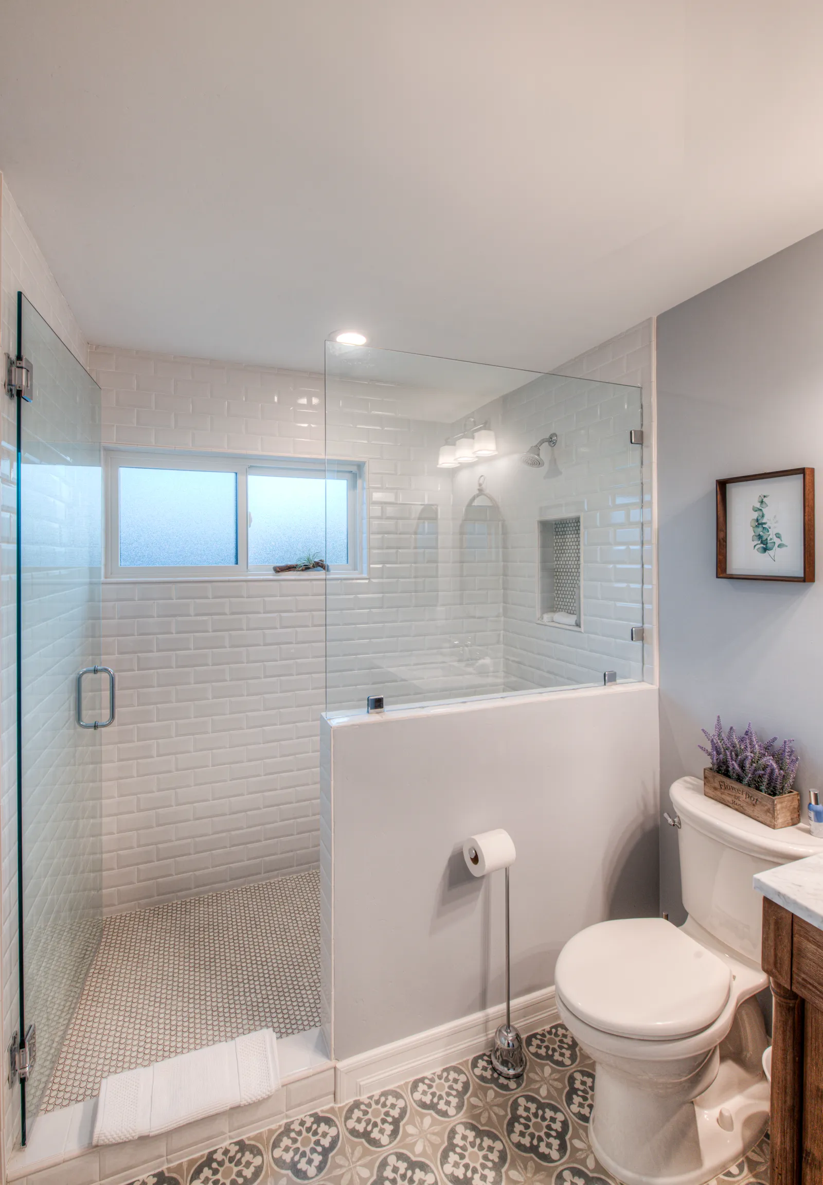 Remodeled bathroom with a glass-enclosed subway tile shower, half wall, and a gray patterned cement tile floor.