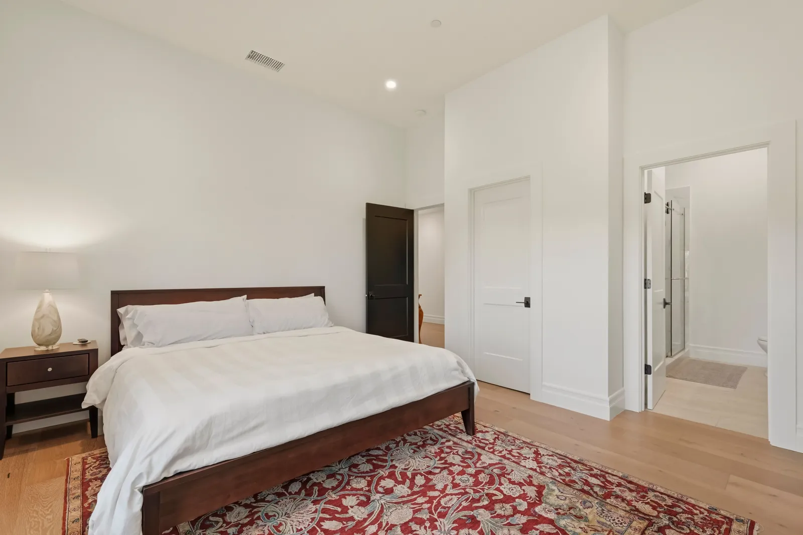 Bedroom with dark wood bed, white bedding, red oriental rug and doorway to an ensuite bath.