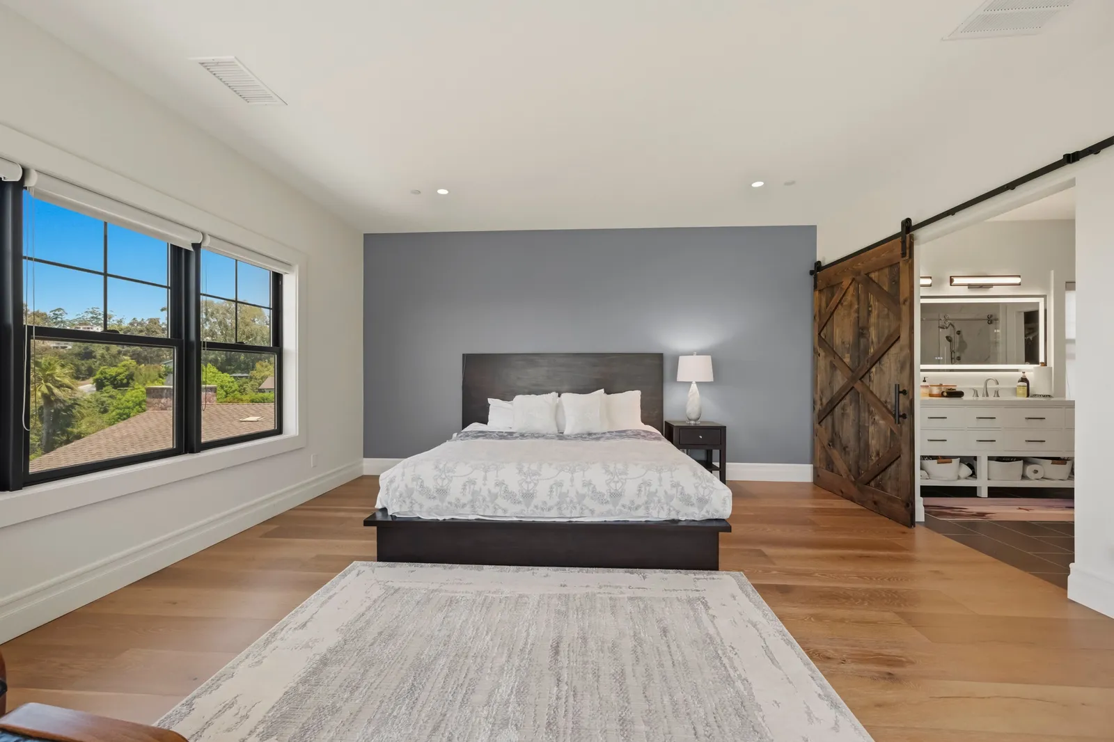 A spacious bedroom with a gray accent wall, platform bed, and sliding barn door opening to a bathroom.