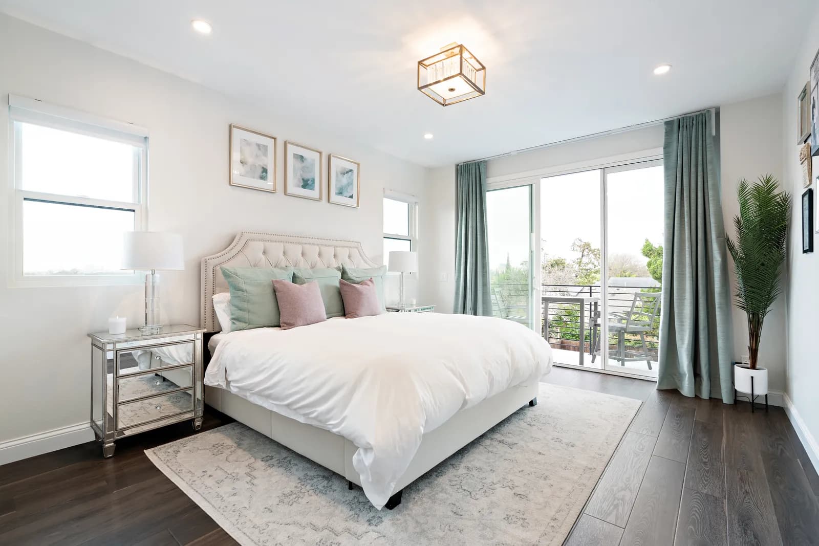 Staged bedroom with tufted headboard, white bedding, green drapes and sliding doors to a balcony.