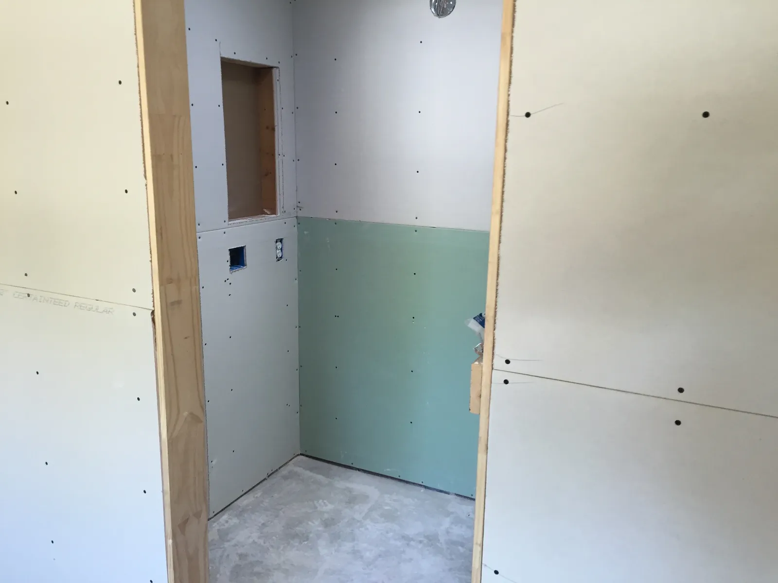Bathroom under construction with fresh drywall, moisture-resistant board, and a roughed-in shower niche.