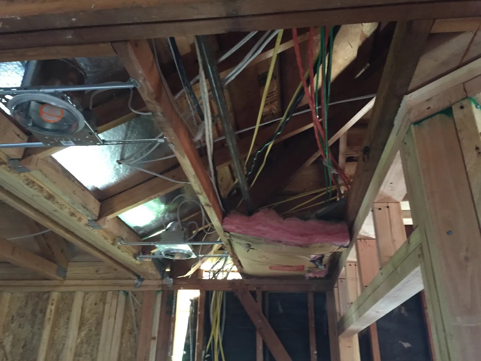 Exposed ceiling framing with electrical wiring, recessed light cans, and insulation during a remodel.