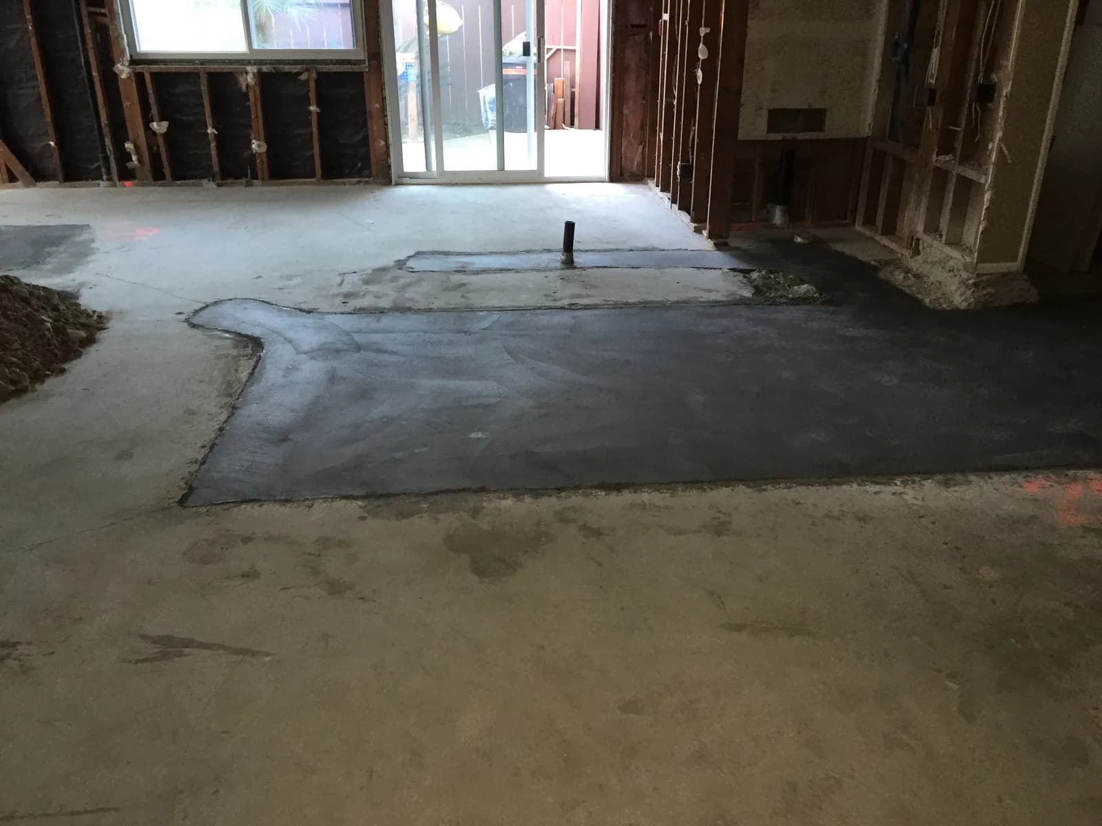 Interior demolition in progress with exposed wall framing and freshly patched concrete slab around new plumbing lines.