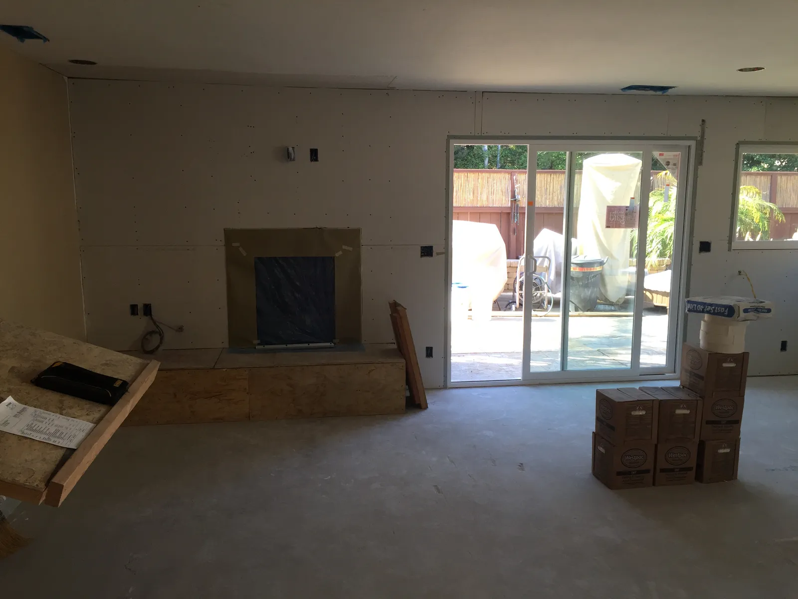 Room mid-remodel with fresh drywall, a covered fireplace opening and sliding glass doors to a patio.