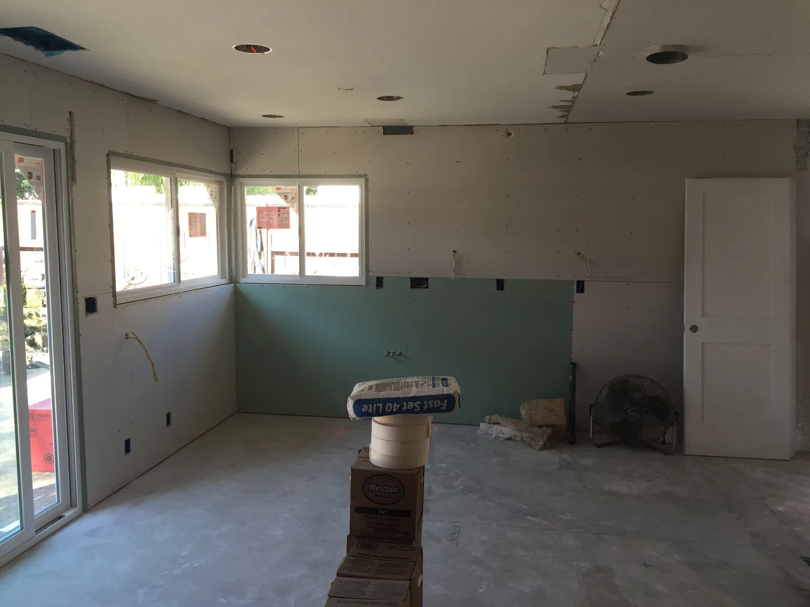 Room under construction with new drywall and green moisture-resistant board installed, buckets and supplies on bare floor.