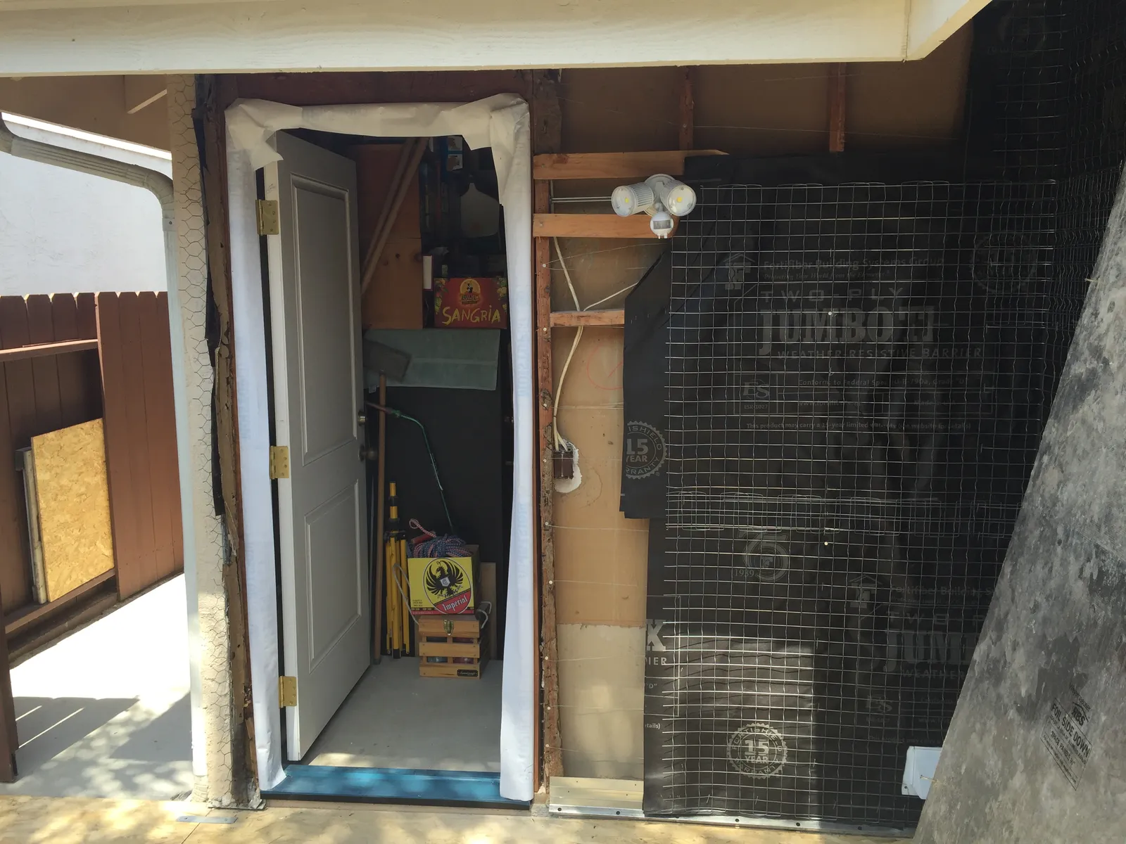 An exterior wall during construction with black weather-resistive barrier and wire lath installed beside an open doorway.