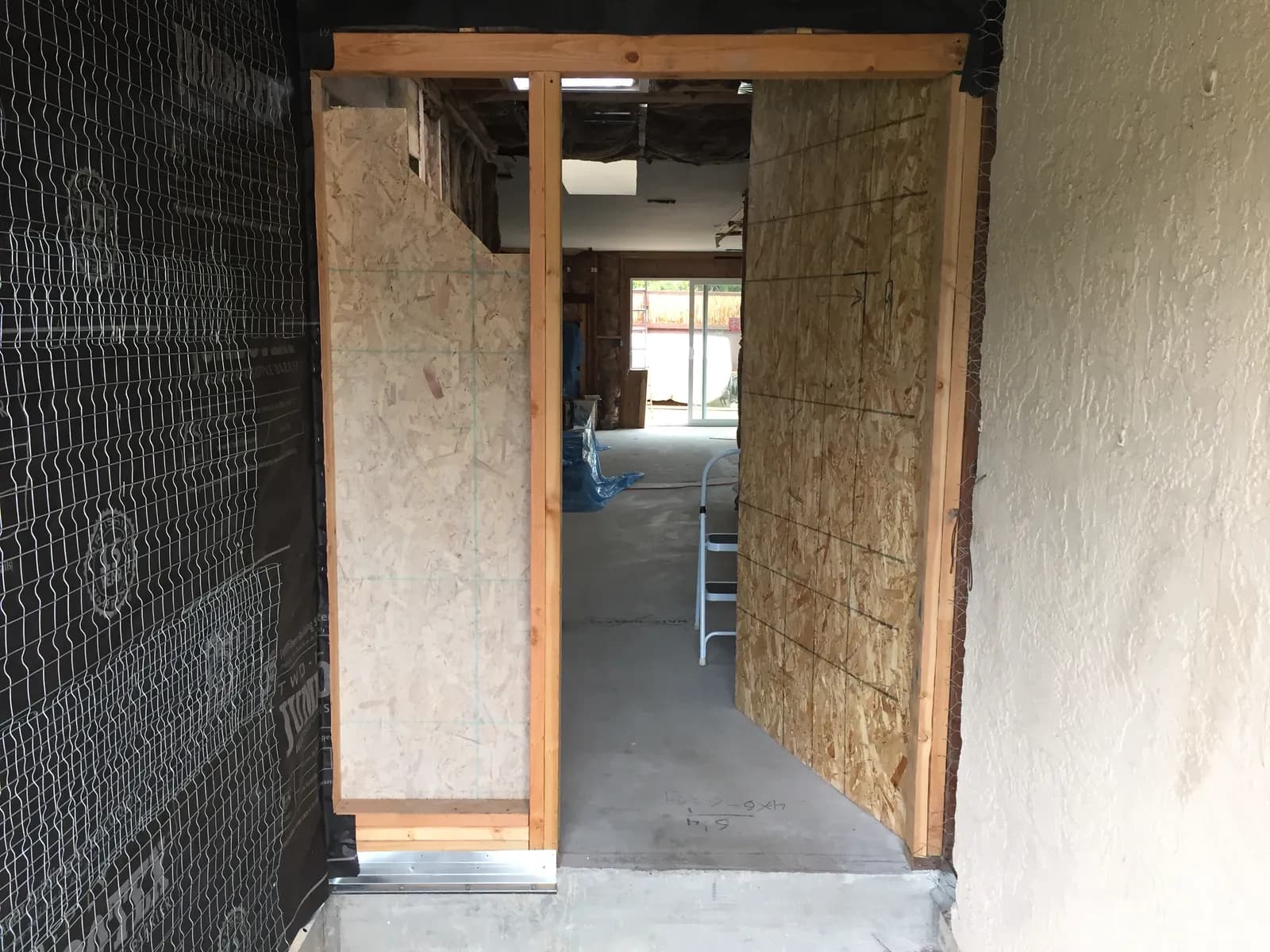 A framed door opening with fresh plywood sheathing and wire lath during interior demolition.