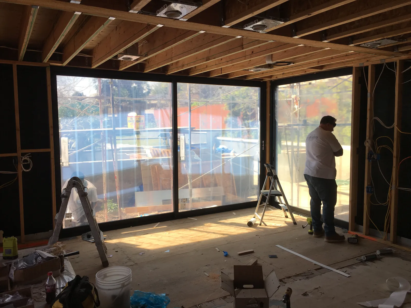 Room under construction with exposed ceiling joists, open framing, wiring, ladders, and new sliding glass doors.
