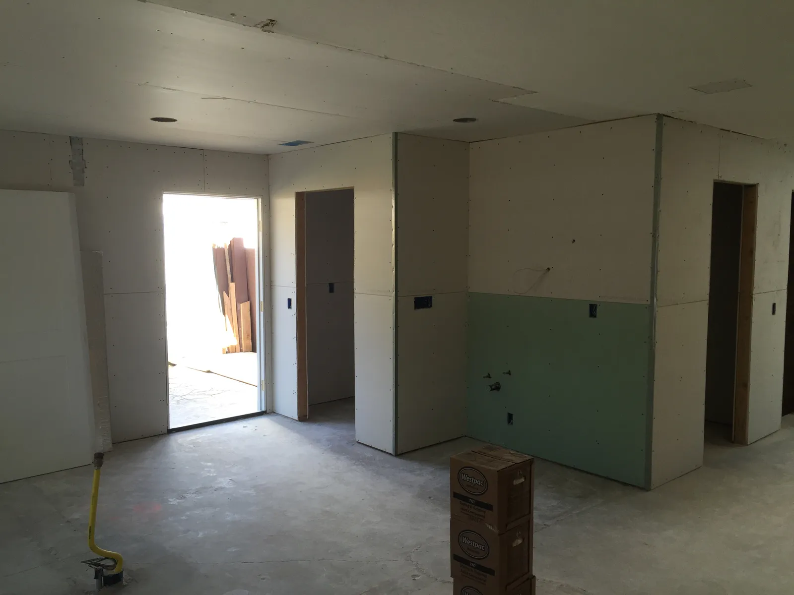 An interior under construction with newly hung drywall, green moisture-resistant board, and boxes of joint compound on the slab.