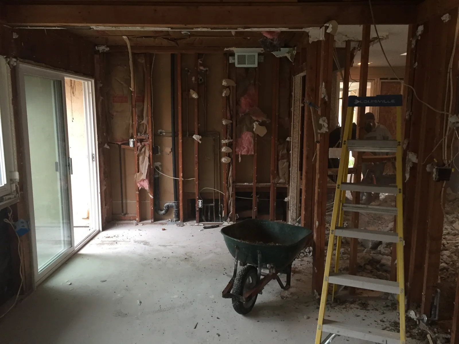 Gutted interior with exposed wall studs, a wheelbarrow of debris, and a yellow step ladder during demolition.