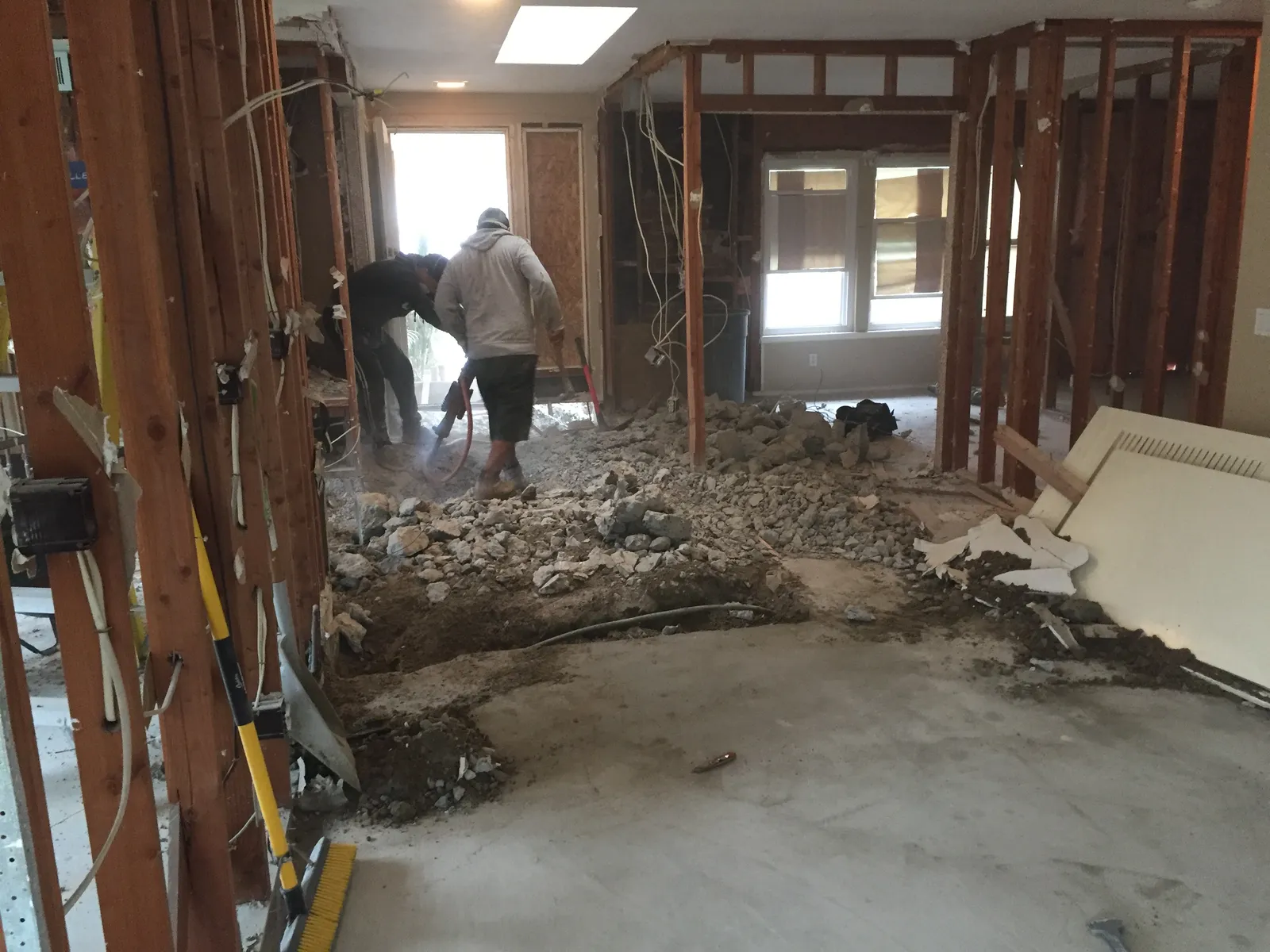 Workers break up a concrete slab inside a house stripped to its wood framing during demolition.