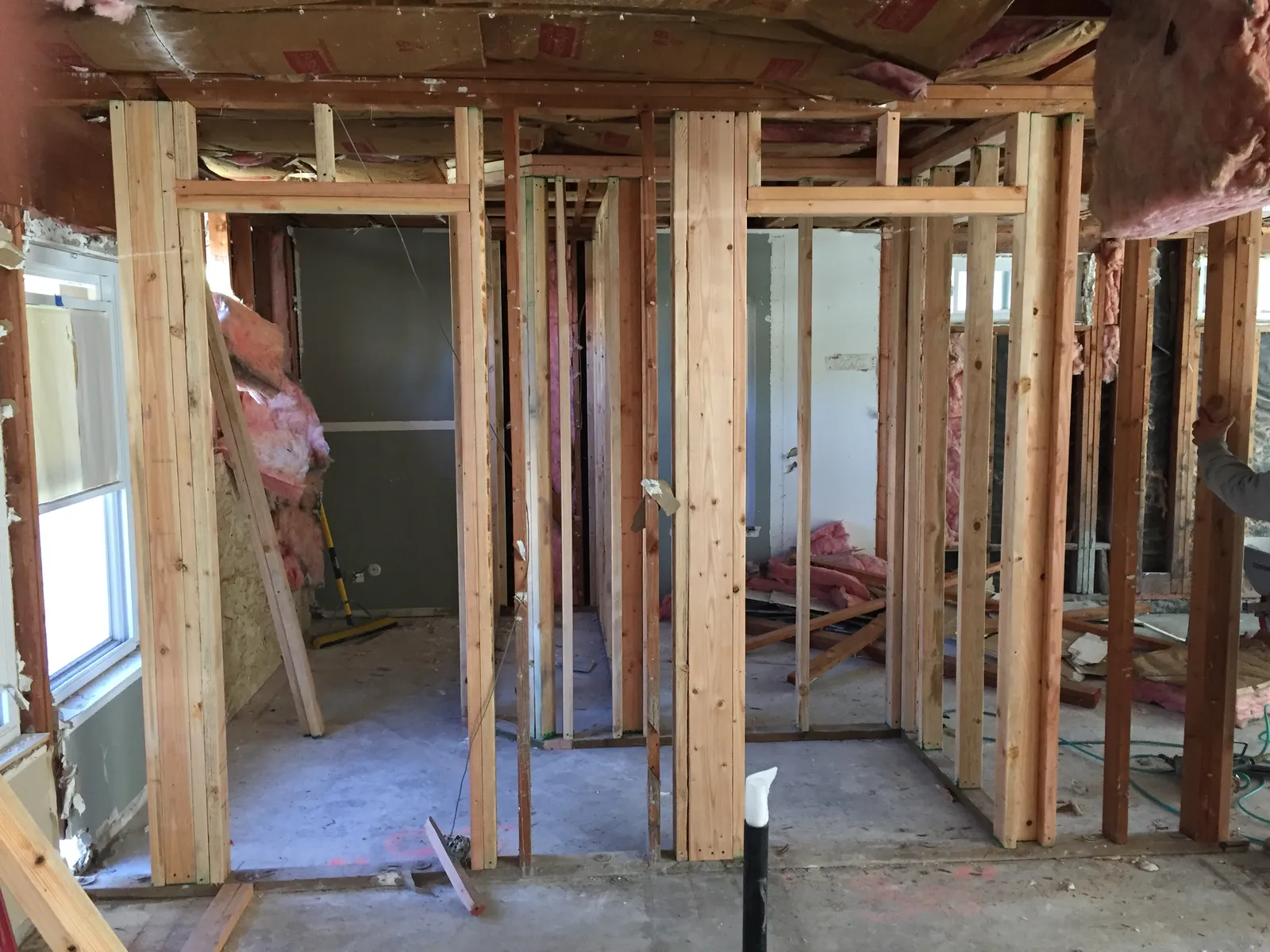 Interior of a home mid-demolition with exposed wood stud framing, insulation, and debris on the floor.