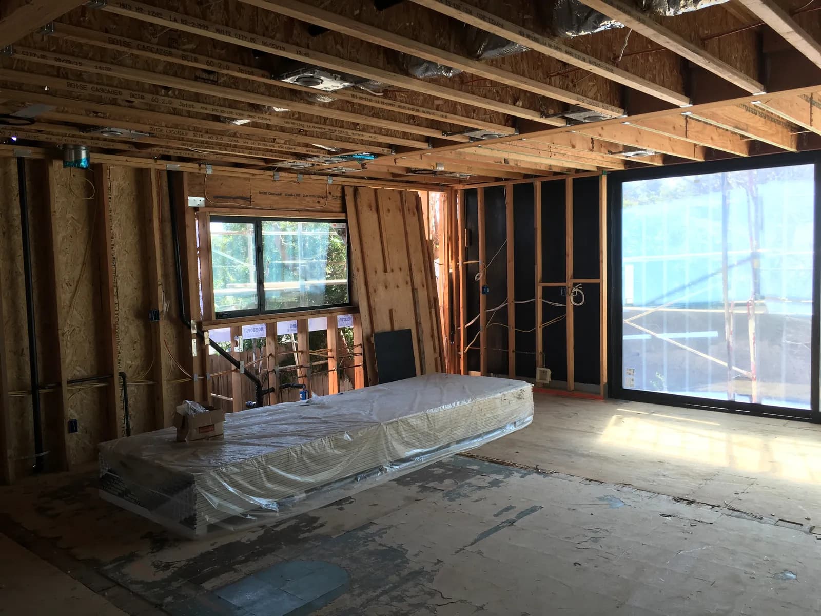 Room under construction with exposed ceiling joists, open stud walls, and stacked drywall on the subfloor.