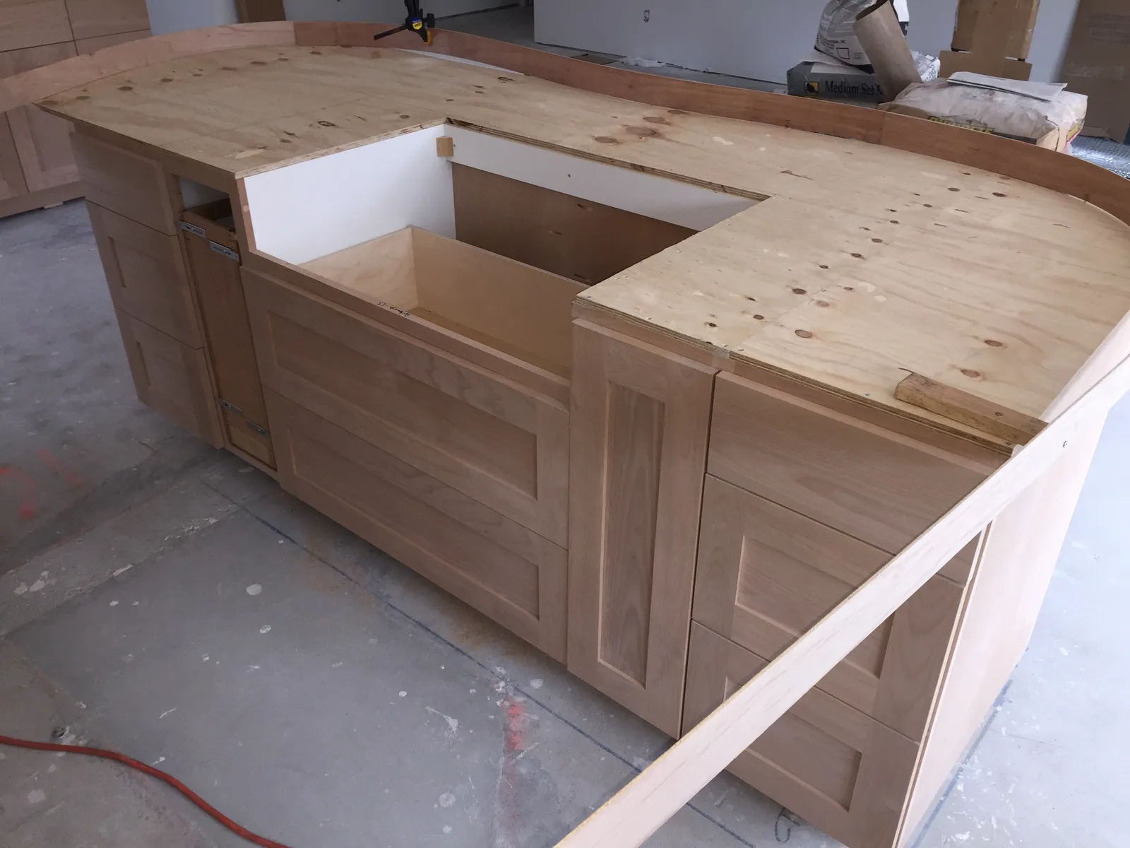Unfinished kitchen island with new cabinet boxes and a curved plywood countertop template during construction.