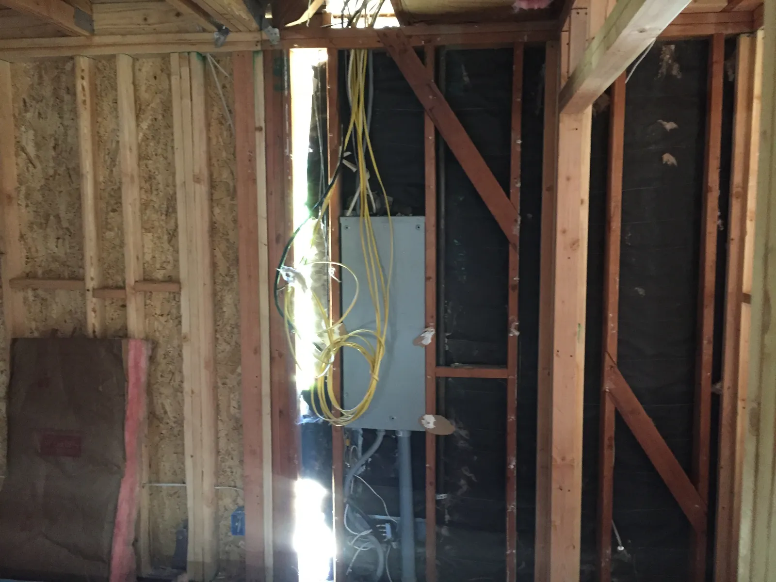 Interior wall framing during construction with an electrical panel, loose wiring, and exposed insulation.