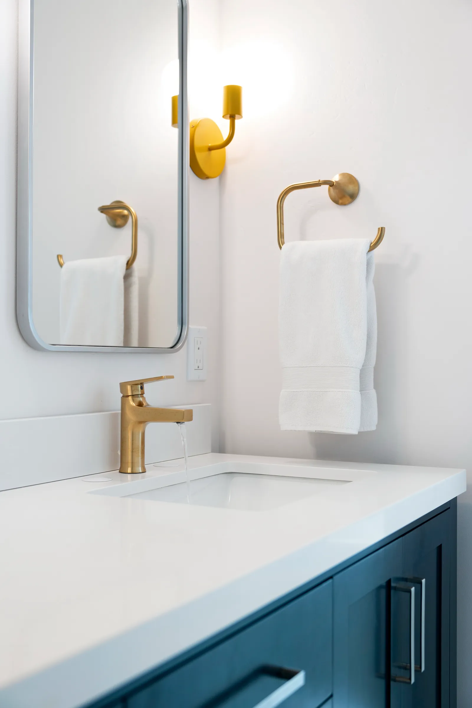 Brass single-handle faucet running on a white quartz vanity top with a navy cabinet below.