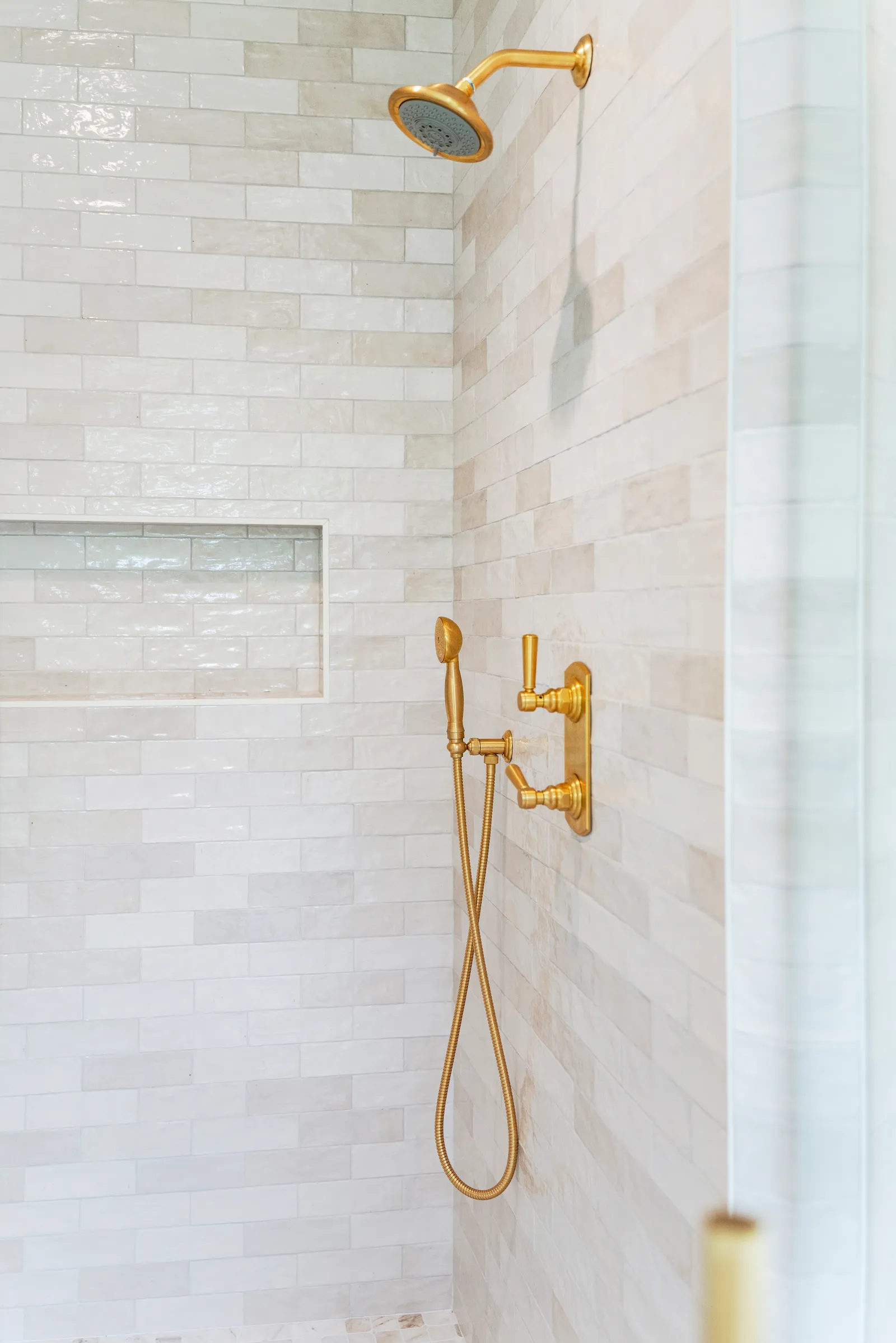 Walk-in shower with handmade-look cream subway tile, brass rain head, hand shower, and a recessed niche.