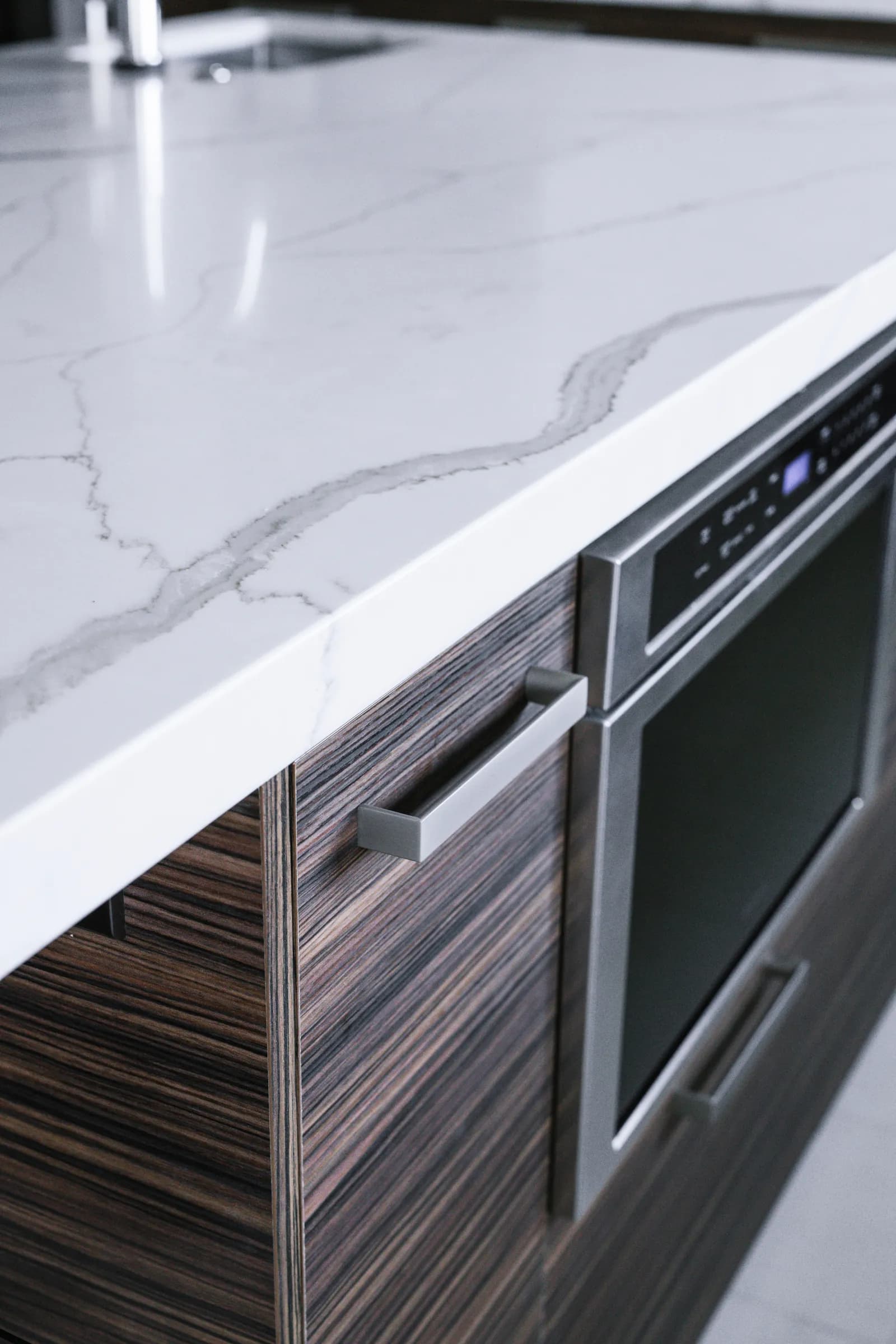 Close-up of a white marbled quartz countertop edge above dark wood-grain island cabinets with a built-in microwave drawer.