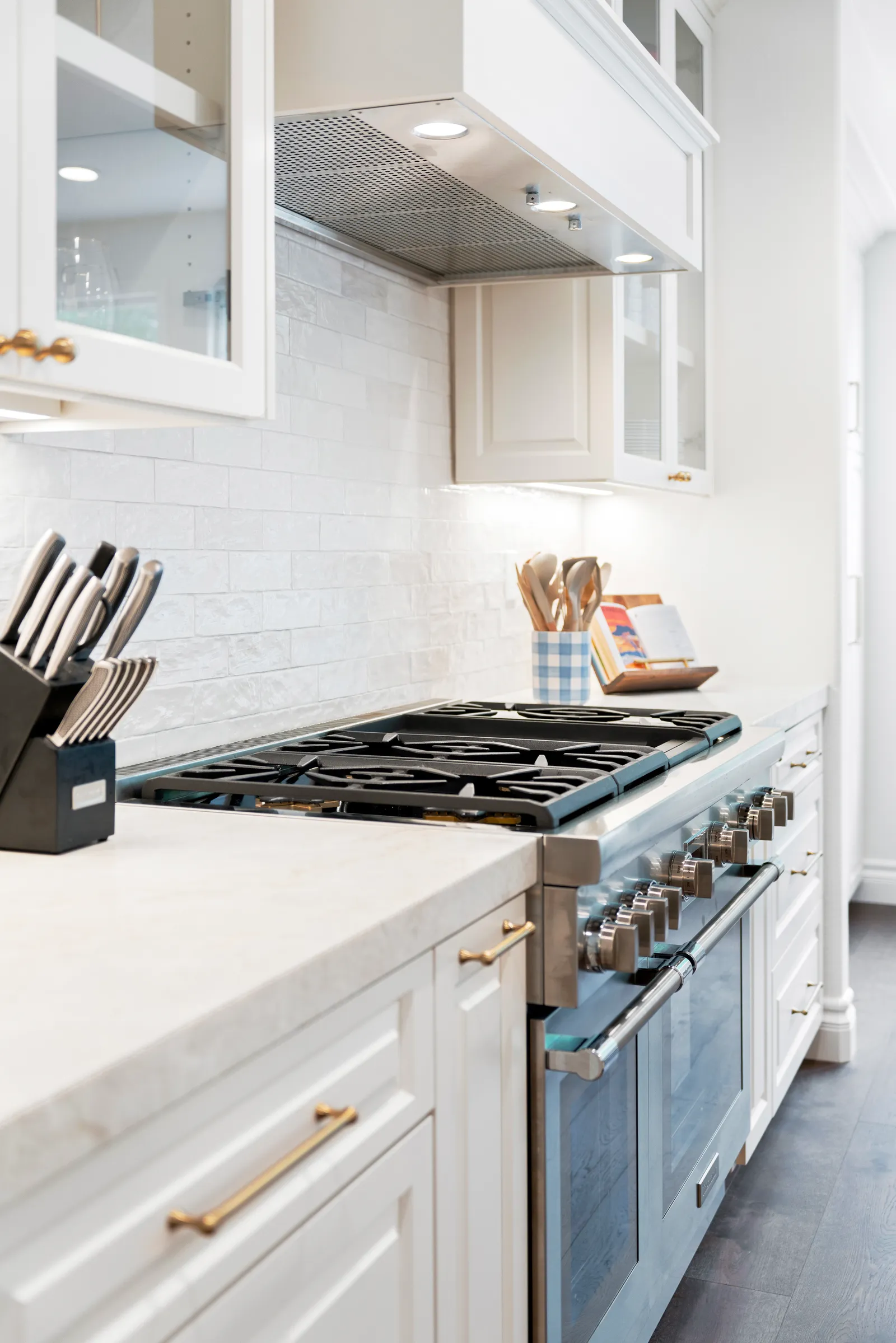 Stainless gas rangetop with cream cabinets, marble counters, brass pulls, and glossy subway backsplash.