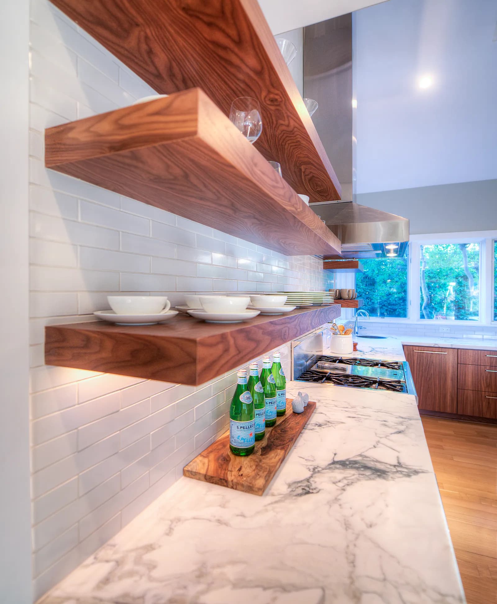 Thick walnut floating shelves with white dishware above a marble counter and subway tile backsplash.