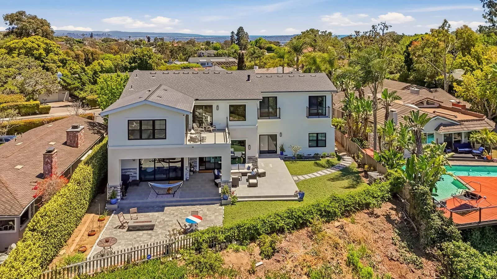 Aerial view of a white two-story home with balconies, patio seating and landscaped backyard.
