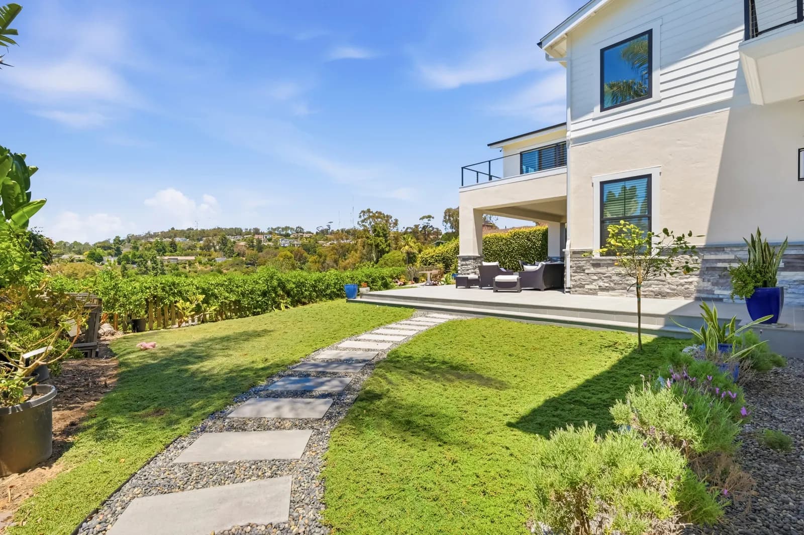 Backyard of a white two-story home with a paver path across the lawn and covered patio seating.
