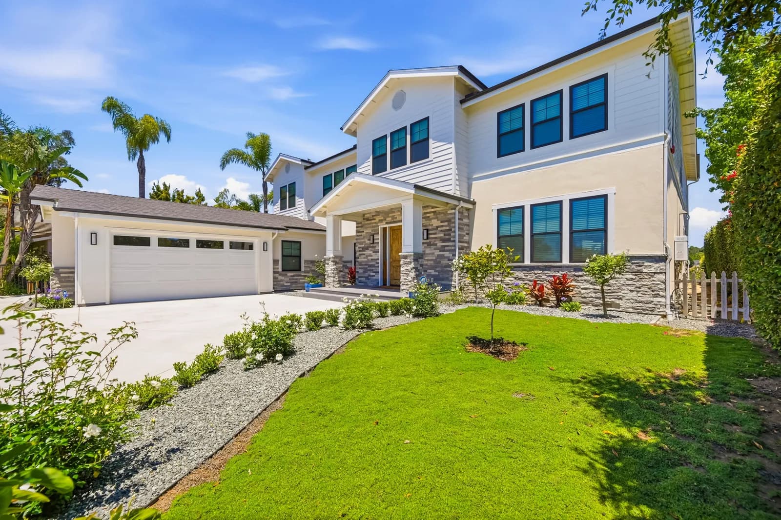 Two-story white home with stacked stone accents, covered entry porch, new lawn, and a wide concrete driveway.