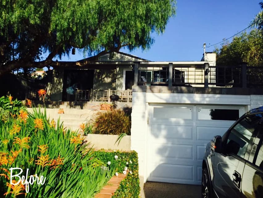 A single-story home with a white garage door, deck railing above, and orange flowering plants in front, with a text overlay reading Before.