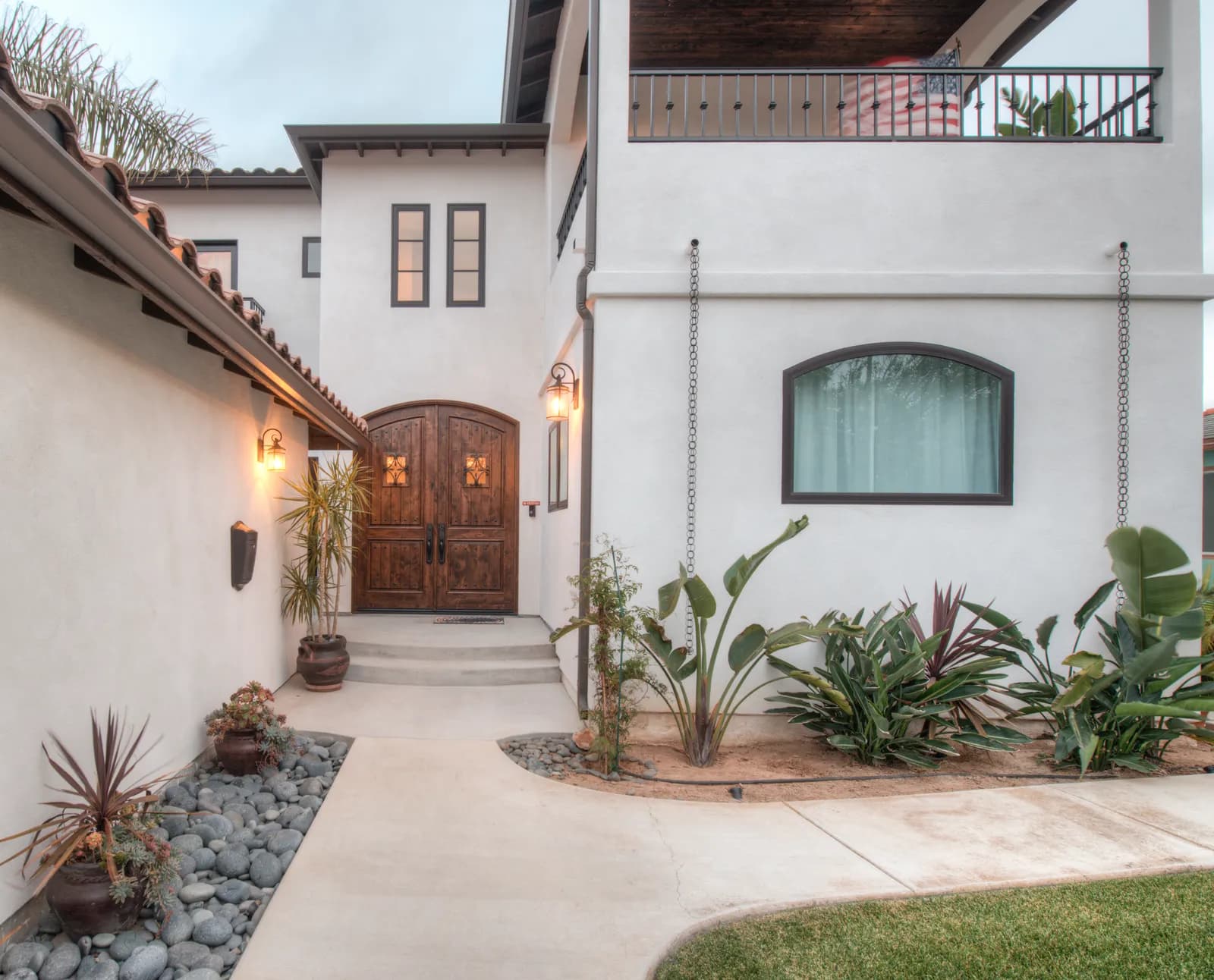 Spanish-style entry courtyard with arched knotty alder double doors, rain chains and tropical plantings.