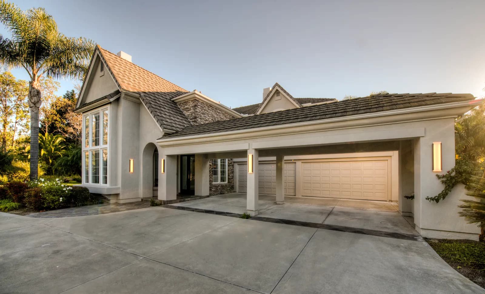 Front exterior of a two-story stucco home with a covered three-car garage and palm trees at dusk.