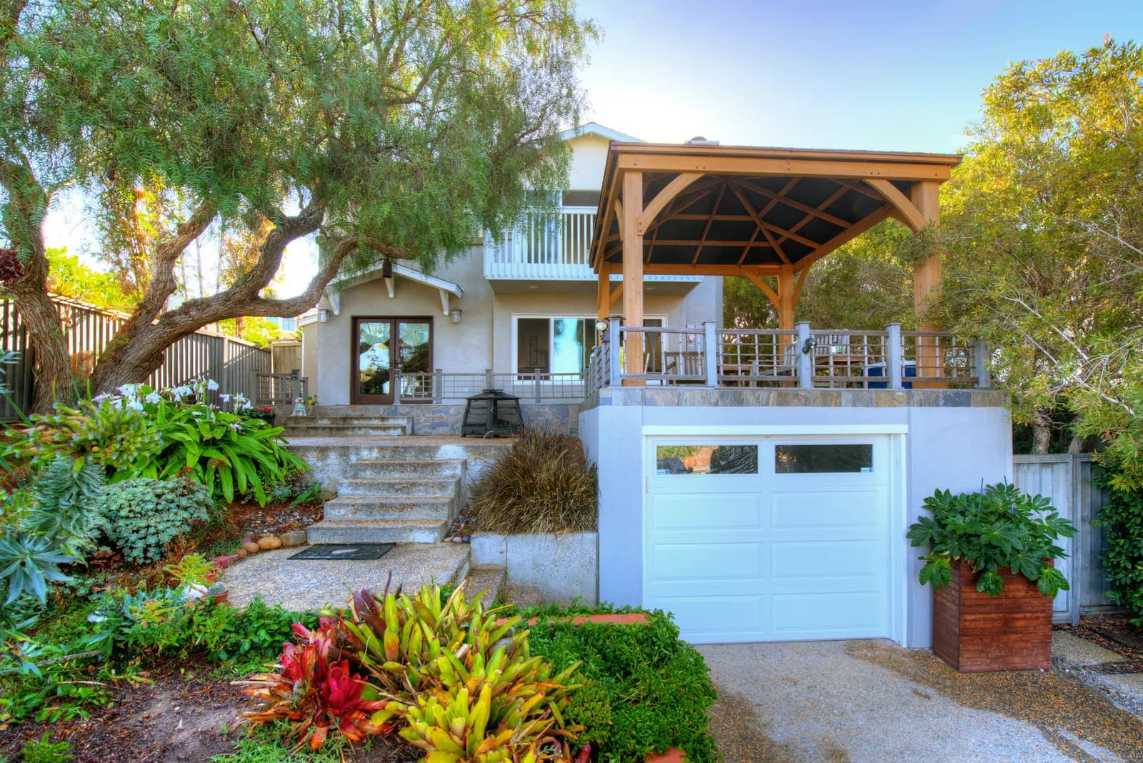 Gray two-story home exterior with a cedar gazebo over the deck, white garage door, and lush landscaping.