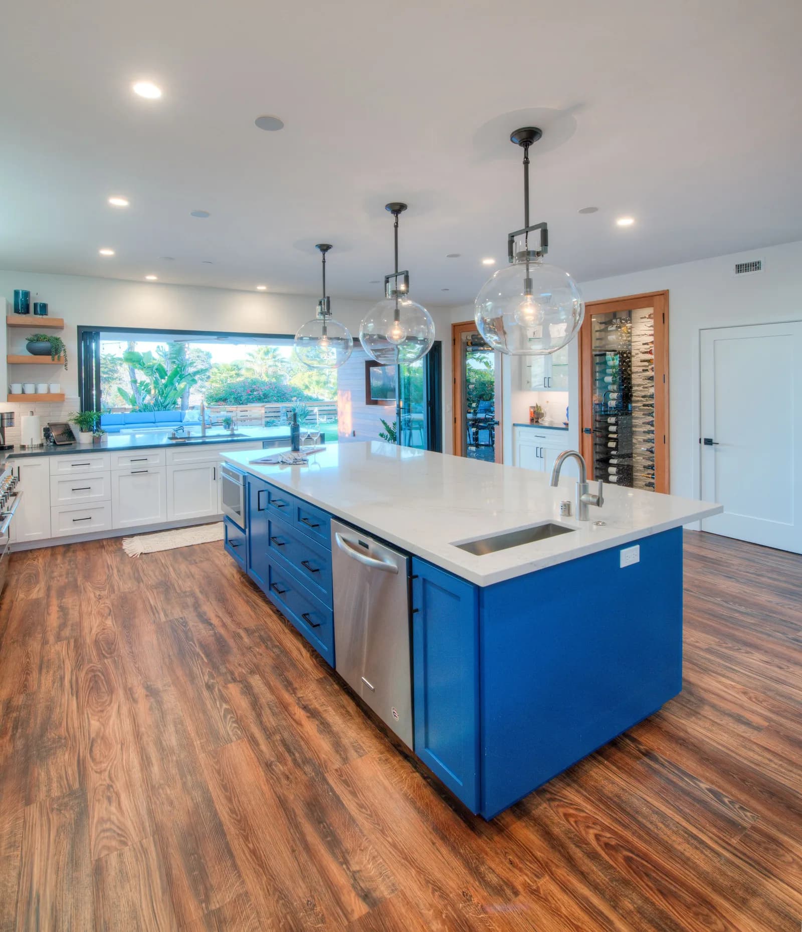 Kitchen with bright blue island, white quartz counters, glass globe pendants, and a glass-front wine display.