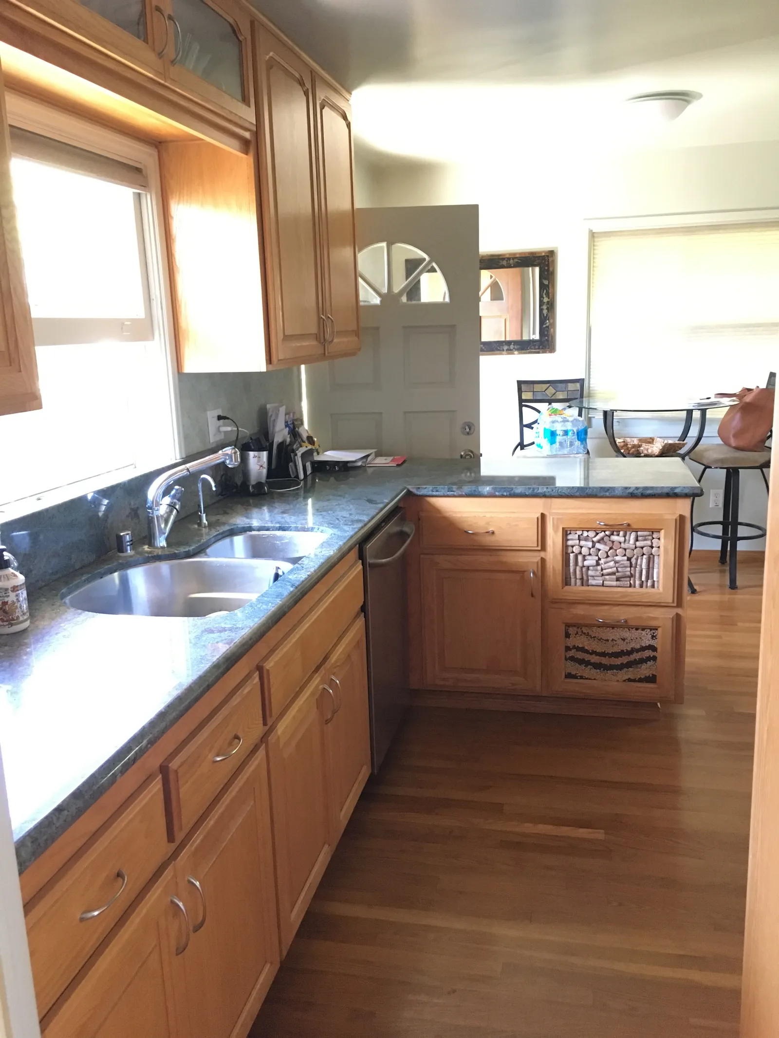 Older kitchen with oak cabinets, green granite counters, double stainless sink and wood floors.