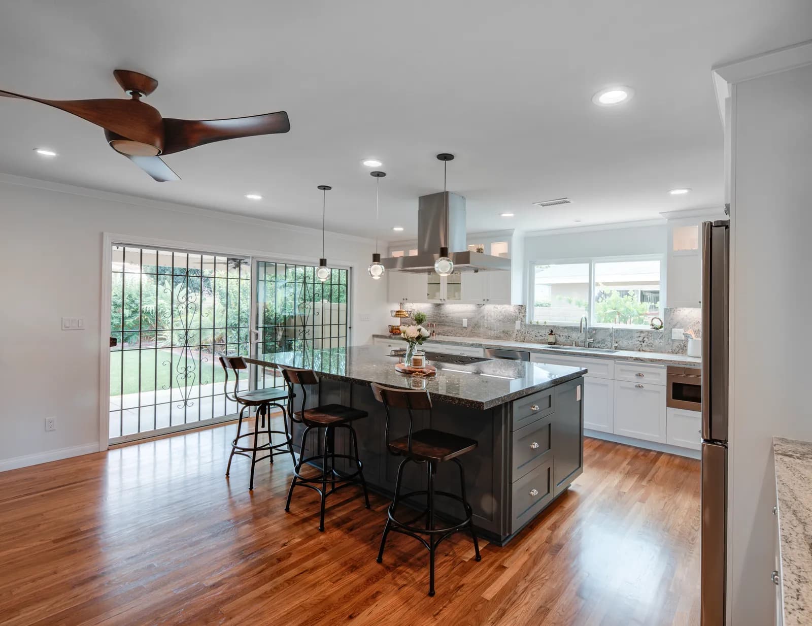 Remodeled kitchen with a charcoal gray island, granite counters, white perimeter cabinets, pendant lights, and red oak flooring.