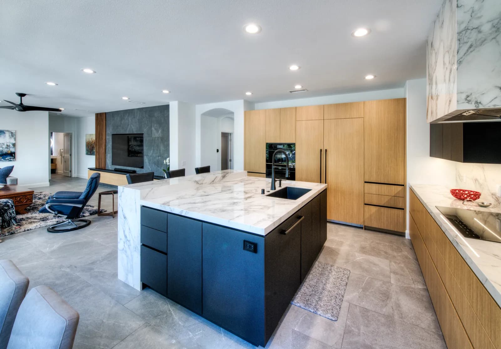 A contemporary kitchen with a marble waterfall island, black island cabinets, white oak tall cabinets, and marble-clad range hood.