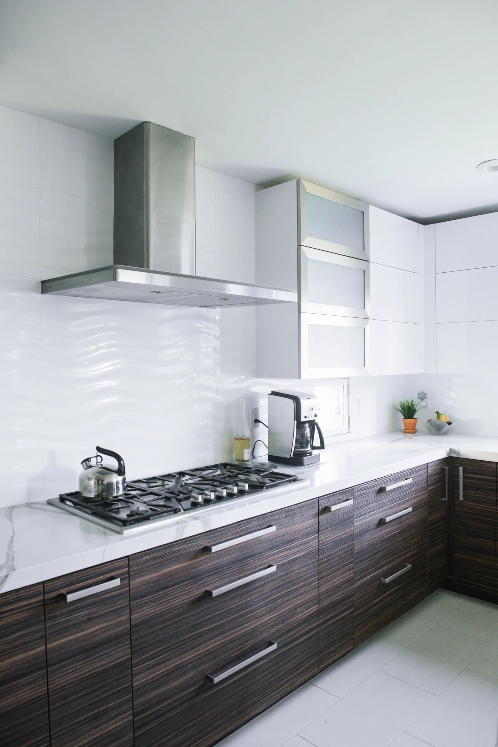 Modern kitchen with dark wood lower cabinets, white counters, gas cooktop, and stainless range hood.