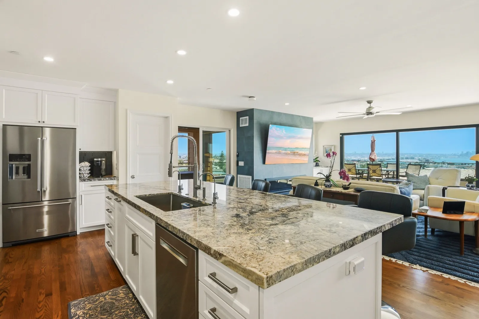 Open-plan kitchen with a large granite island flowing into a living area with panoramic city and bay views.